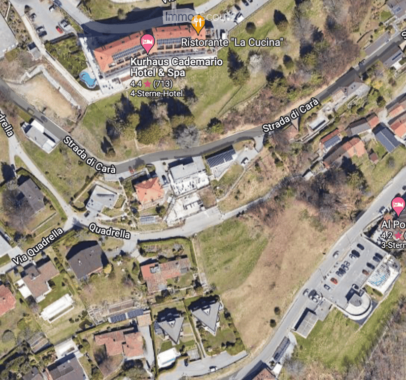 Aerial view of a residential area with multiple buildings, roads, and a swimming pool visible.