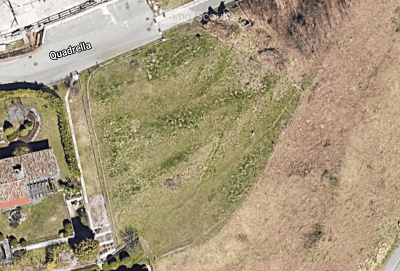 Aerial view of a rural area with a small building, a circular driveway, and surrounding grassy and bare land.