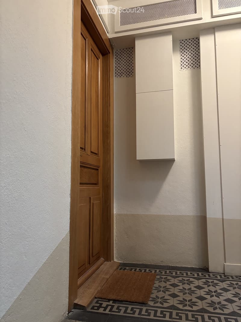 Hallway with patterned tile floor, white walls, wooden door frame, and a small doormat.