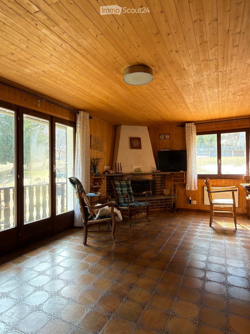 Cozy living room with wooden walls, slanted ceiling, fireplace, large windows, and comfortable seating.