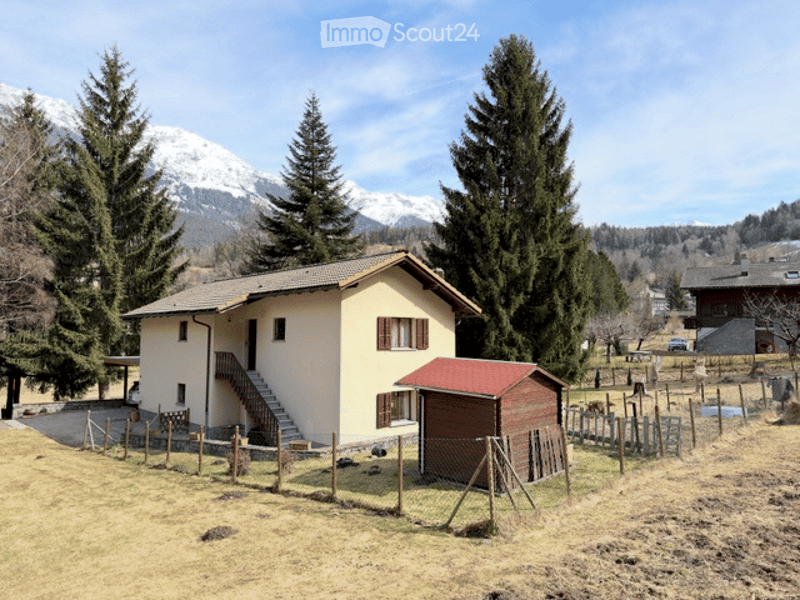 Single-story house with a red roof and white walls, surrounded by trees and mountains. Includes a small wooden shed and fenced yard.