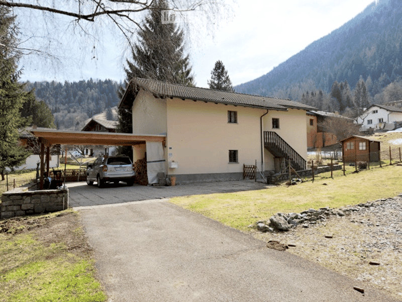 Two-story house with a garage, surrounded by trees and mountains, with a driveway leading to the entrance.