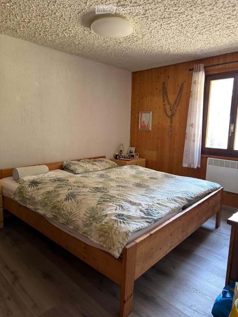 Cozy bedroom with wooden bed, nightstand, lamp, and picture frame on wooden wall.