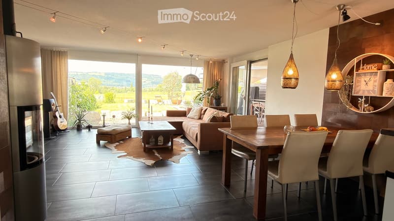 Open-plan living and dining area with a sofa, coffee table, dining table, chairs, guitar, candles, potted plants, and decorative shelves.