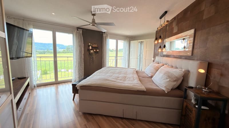 Modern bedroom with a large bed, nightstands, a ceiling fan, and large windows offering a scenic view.
