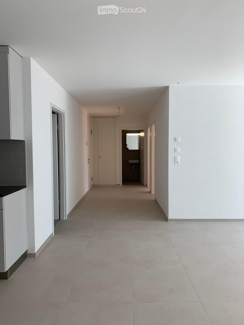 Empty hallway with tiled floor, white walls, and a closed door leading to a small bathroom visible at the end.