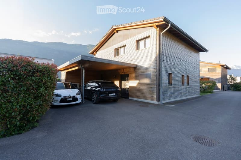 Modern two-story house with a covered garage, two parked cars, and a view of mountains in the background.