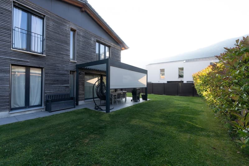 Well-maintained garden with a modern patio area, outdoor furniture, and a covered seating area attached to a contemporary house.