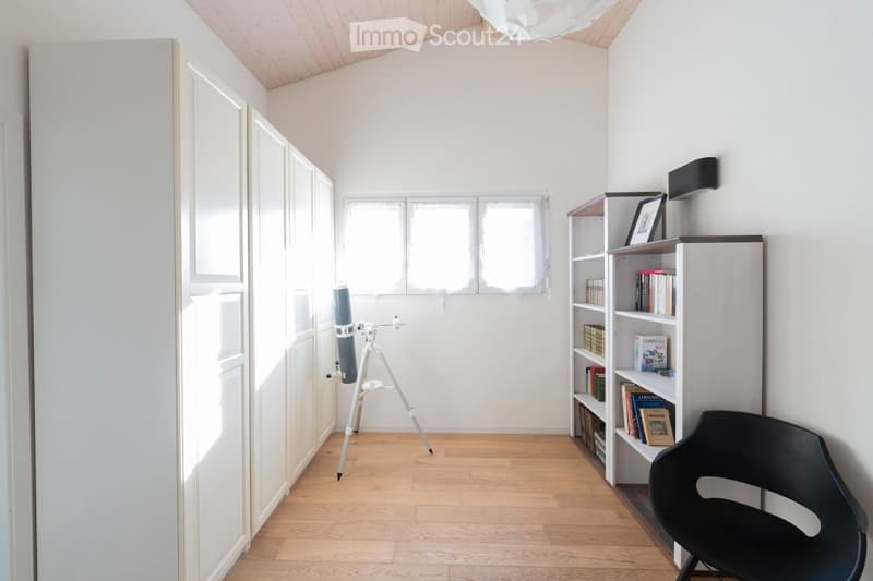 Bright room with wooden floor, large windows, bookshelf, telescope, and a modern chair.
