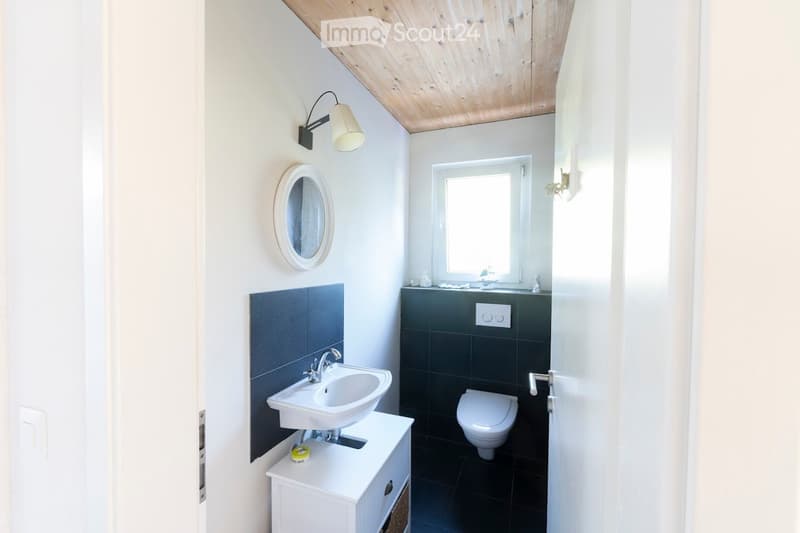 Modern bathroom with white sink, toilet, dark tiles, and a round mirror above the sink.