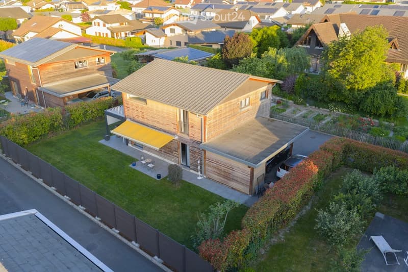 Aerial view of a modern two-story house with a garage, surrounded by a well-maintained garden and neighboring houses.