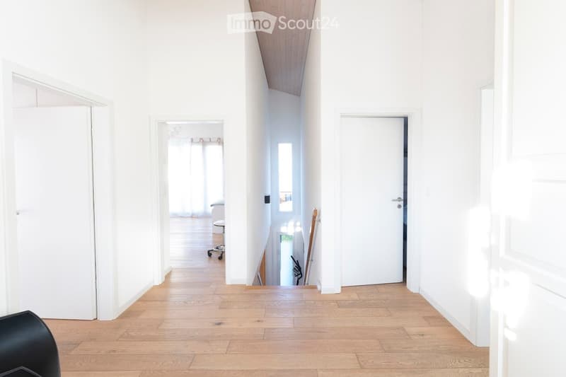 Bright, minimalist hallway with light wooden flooring, white walls, and several doors leading to other rooms.