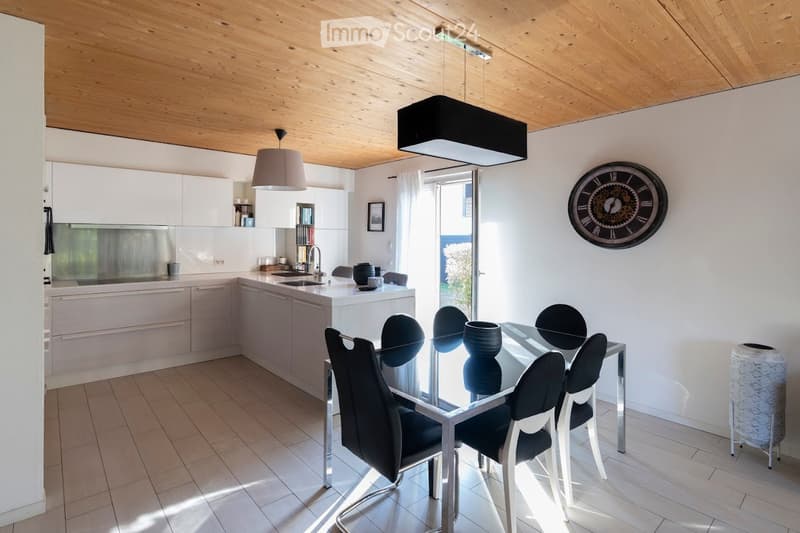 Modern kitchen with white cabinets, a central island, pendant lights, and a dining area with a glass table and black chairs.