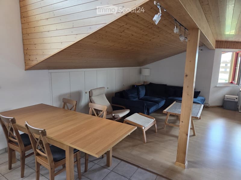 Bright living room with wooden ceiling, white cabinets, sofa, dining table, chairs, and a small table with a lamp.