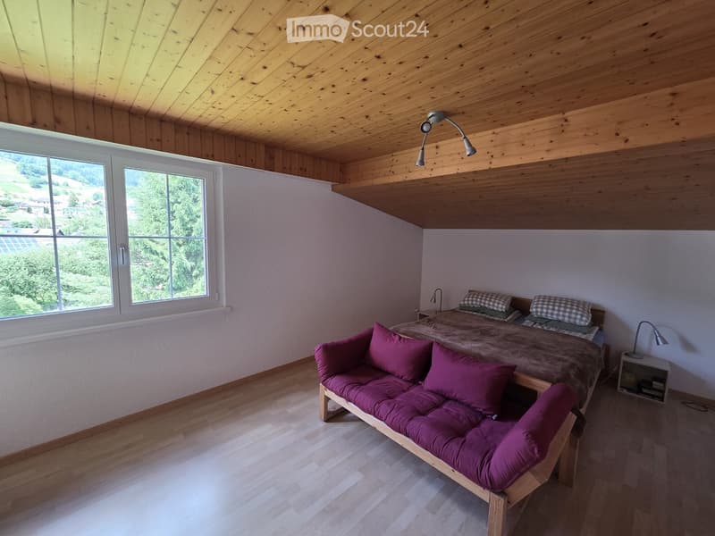 Cozy bedroom with wooden ceiling and walls, large windows with scenic view, sofa bed, double bed, nightstand, and lamps.
