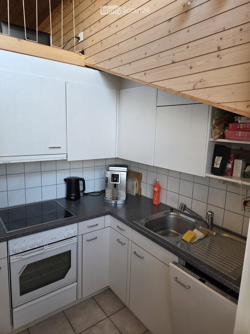 Modern kitchen with white cabinets, black countertops, and stainless steel sink. Features an oven, coffee maker, and various kitchen items on the counter.