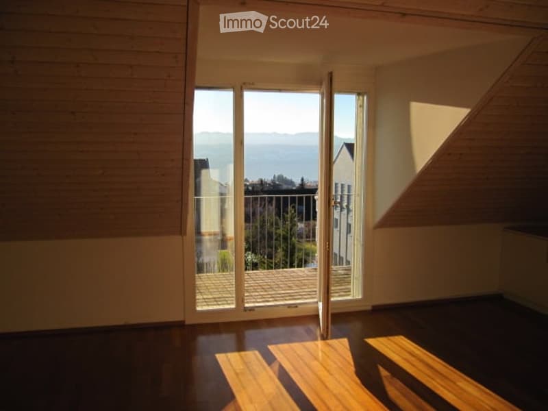 Open sliding glass doors lead to a balcony with a scenic view of the landscape and surrounding buildings.