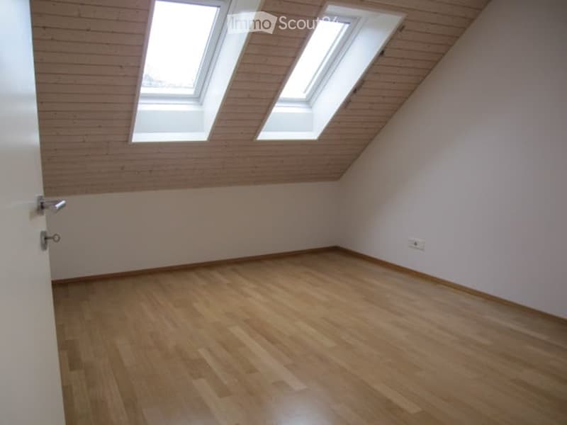 Empty attic room with wooden flooring, white walls, and skylight windows.