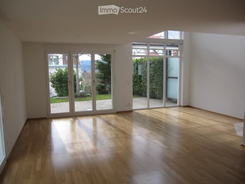 Empty room with wooden flooring and large glass sliding doors leading to a garden view.