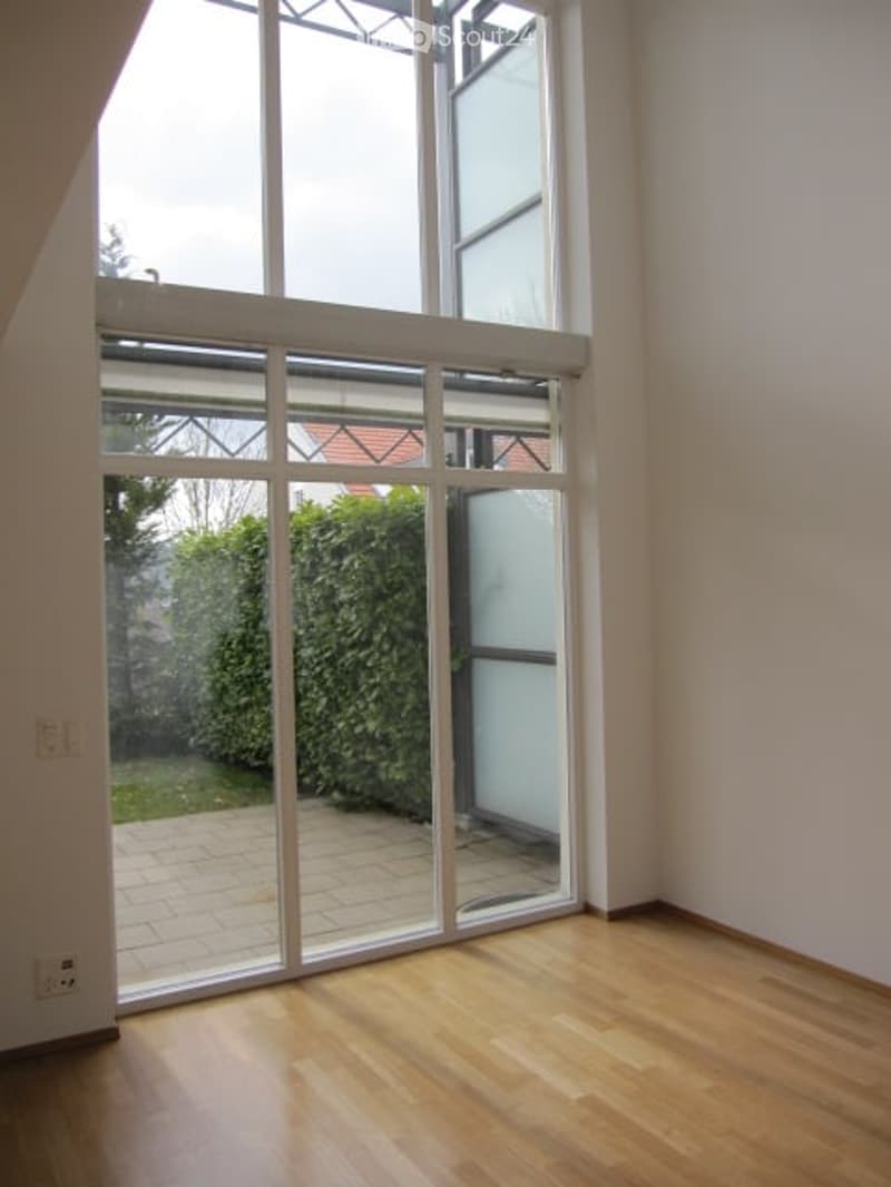 Empty room with wooden flooring, large glass sliding doors leading to a patio area, and white walls.