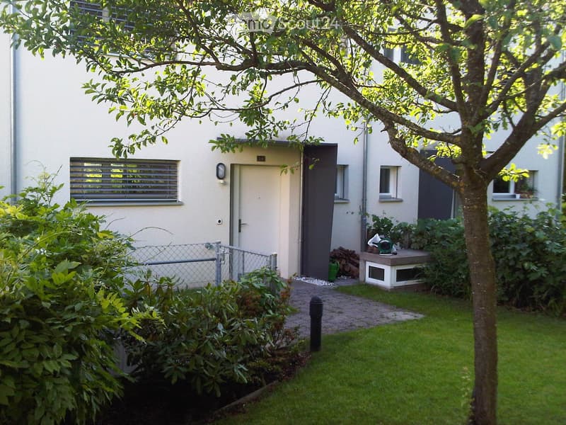 Garden area with a small tree, lawn, shrubs, a small shed, and a pathway leading to the house entrance.