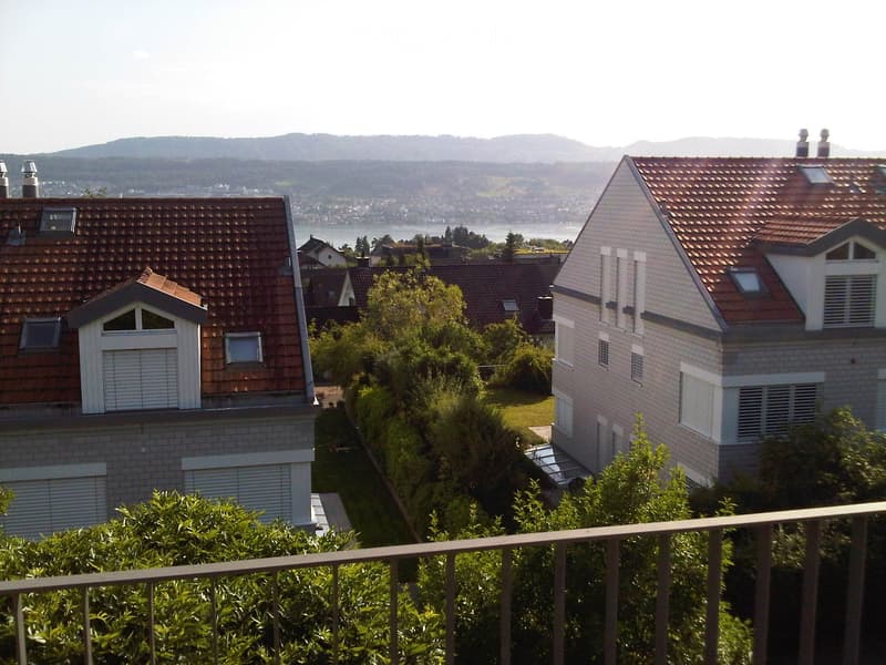 View of two houses with red-tiled roofs and white walls, surrounded by greenery and overlooking a body of water and distant hills.