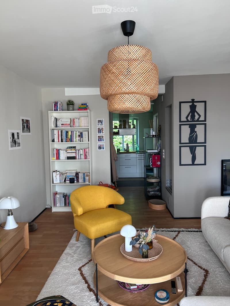 Modern living room with a yellow armchair, white sofa, round wooden coffee table, bookshelf, and decorative items.