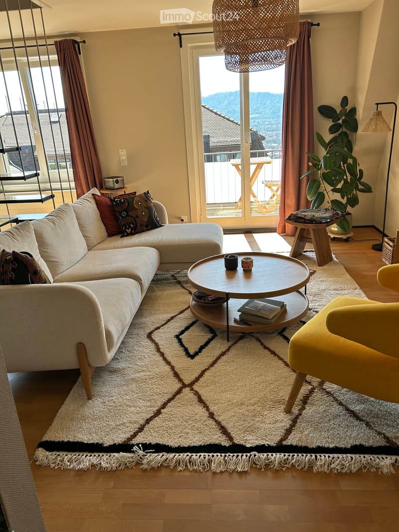 Modern living room with a sectional sofa, coffee table, armchair, and large windows offering a scenic view.