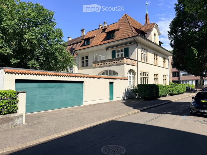 Two-story house with a red-tiled roof, multiple windows, and a green garage door.