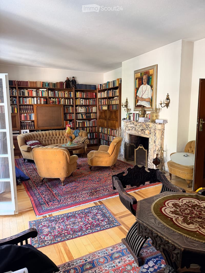 Elegant living room with a cream-colored sofa, armchairs, coffee table, bookshelves, fireplace, and ornate wooden table.