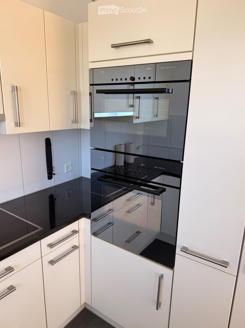 Modern kitchen with white cabinets, stainless steel oven, and black countertop.