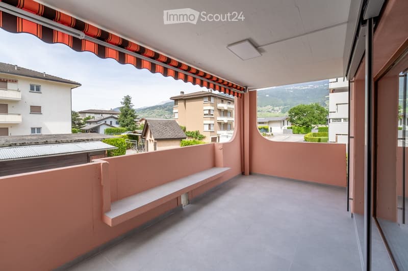 Balcony with pink walls, tiled floor, and a bench, overlooking a scenic mountain view.