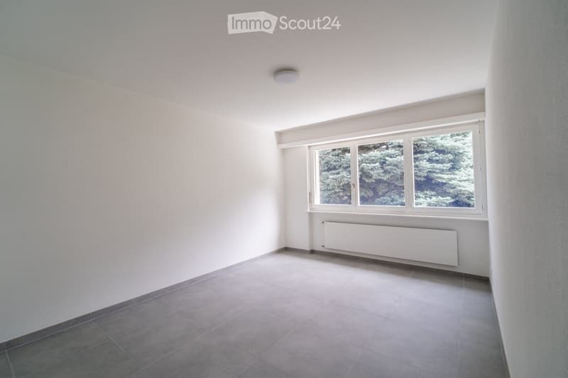 Empty room with white walls, tiled floor, large window with white frame, and a white radiator below the window.