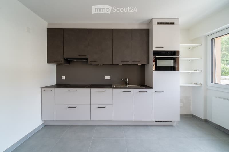 Modern kitchen with white and dark grey cabinets, a sink, a faucet, and an oven. The space is clean and well-lit with grey tiled flooring.