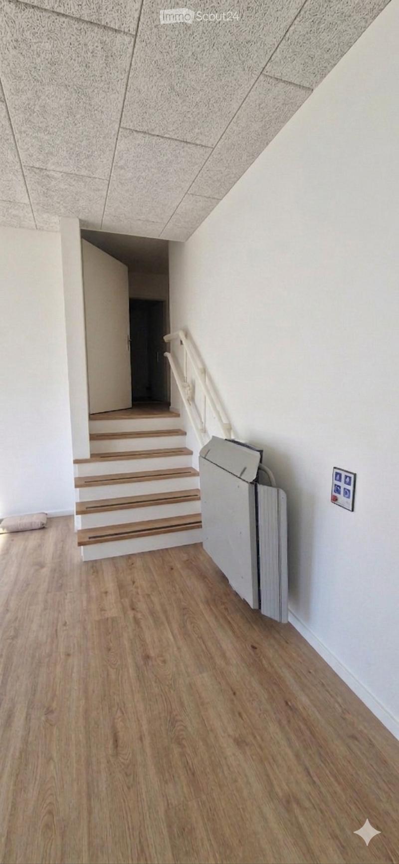 Empty hallway with wooden flooring, white walls, and a staircase leading upwards. A radiator is visible on the right side.