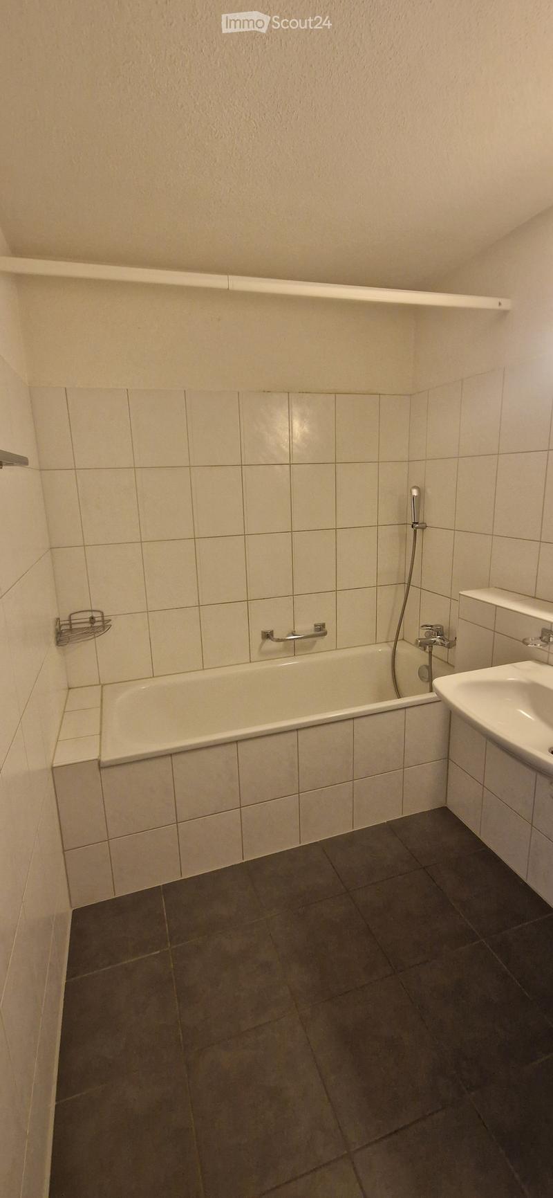 Bathroom with a bathtub, sink, and showerhead, featuring tiled walls and a dark tiled floor.