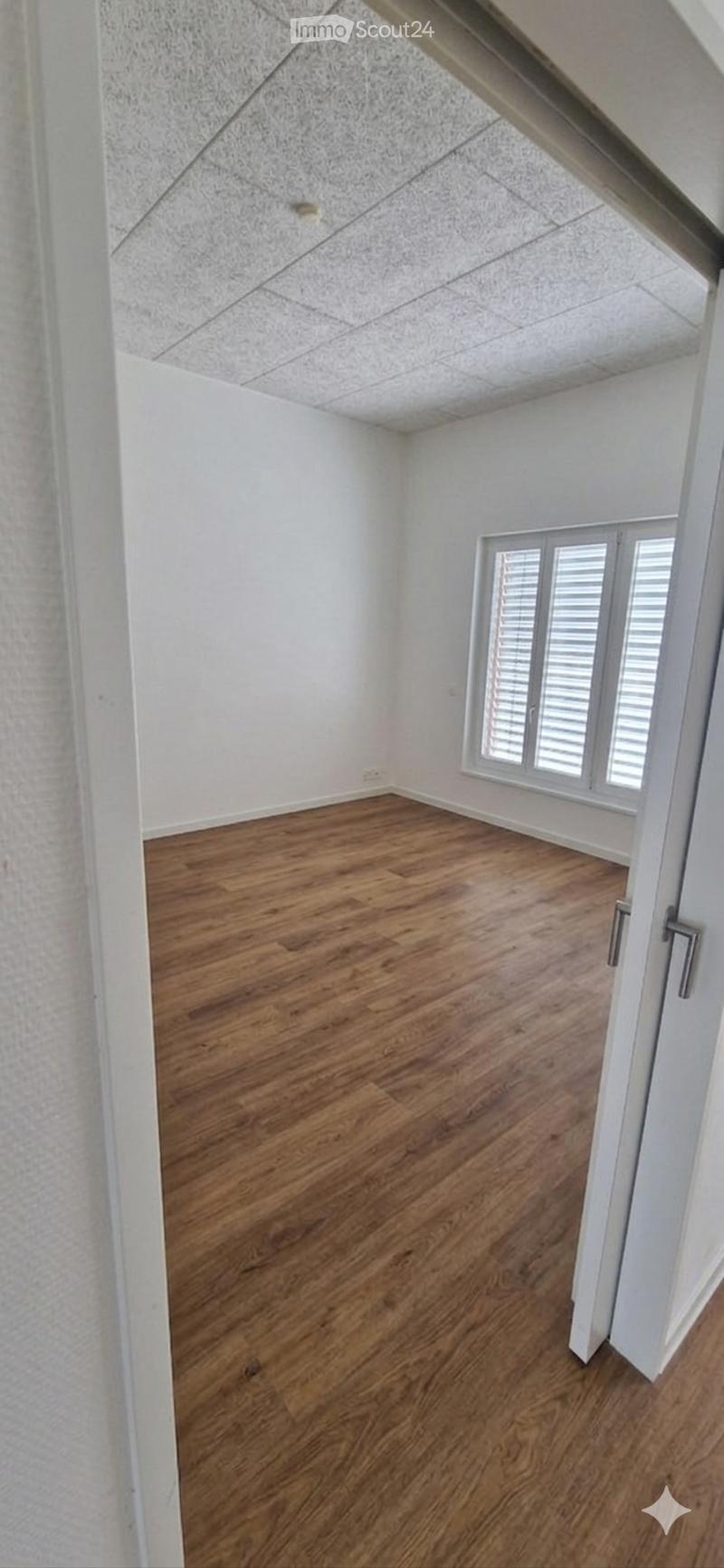 Empty room with wooden flooring, white walls, and a large window with blinds.