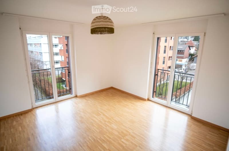 Empty room with wooden flooring, large sliding glass doors leading to a balcony, and a hanging woven light fixture.