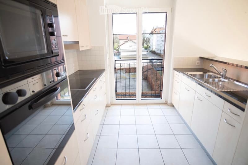 Modern kitchen with white cabinets, tiled floor, microwave, oven, sink, and a sliding glass door leading to a balcony.