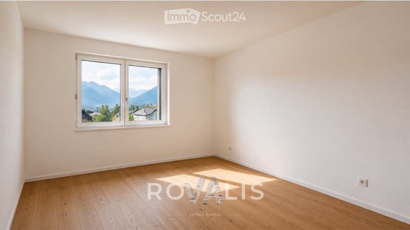 Empty room with light-colored walls and wooden flooring, featuring a large window with a scenic mountain view.