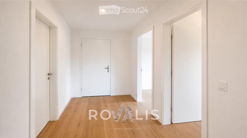 Empty hallway with wooden flooring, white walls, and multiple doors.