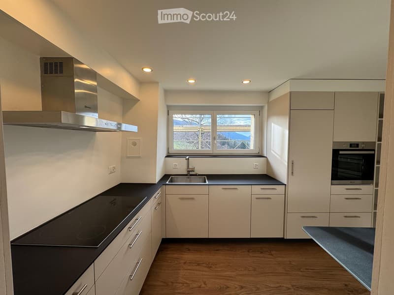 Modern kitchen with light-colored cabinets, black countertops, a built-in stove, sink, and oven. Features a large window with a view of the outdoors.