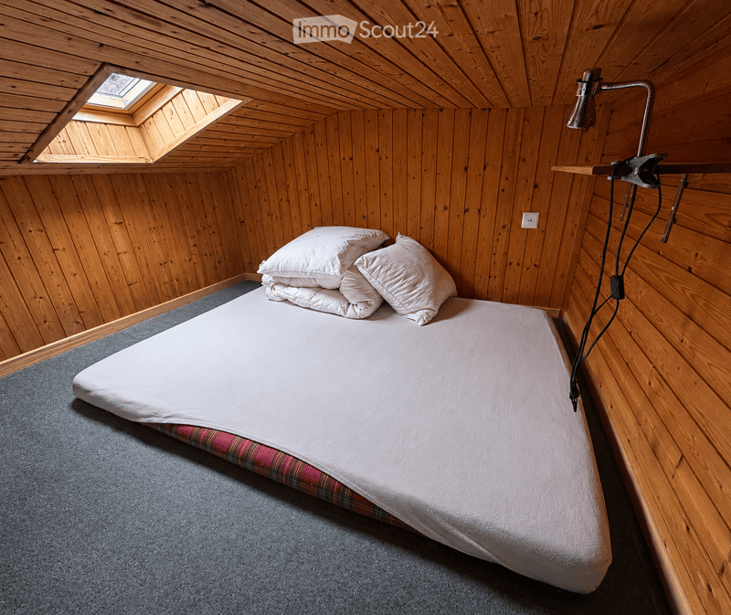 Cozy wooden bedroom with a single bed, white pillows, and a plaid bedspread, featuring wooden walls and a skylight window.
