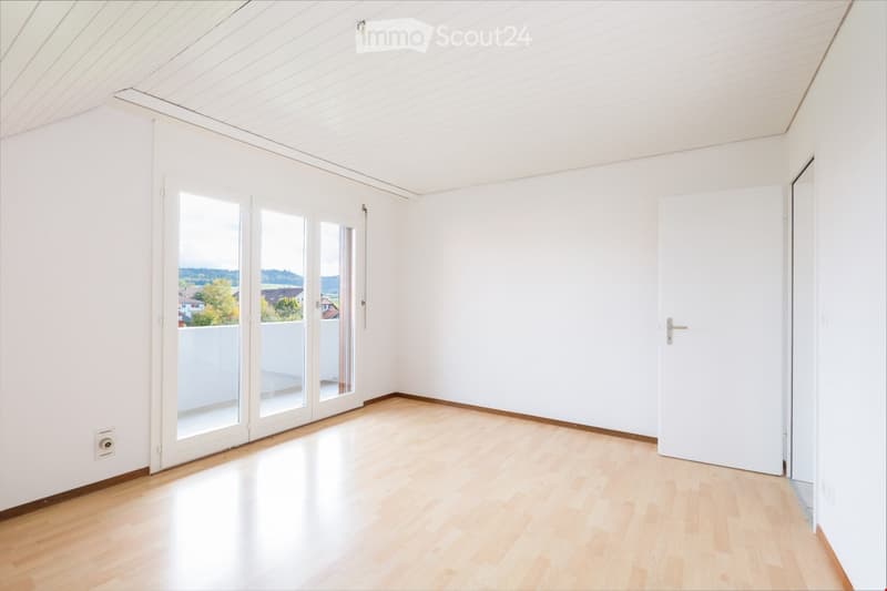 Empty room with white walls, light wooden flooring, and large sliding glass doors leading to a balcony.