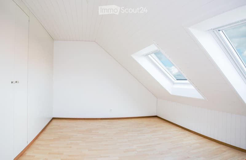 Empty attic room with wooden flooring, white walls, and skylight windows allowing natural light.
