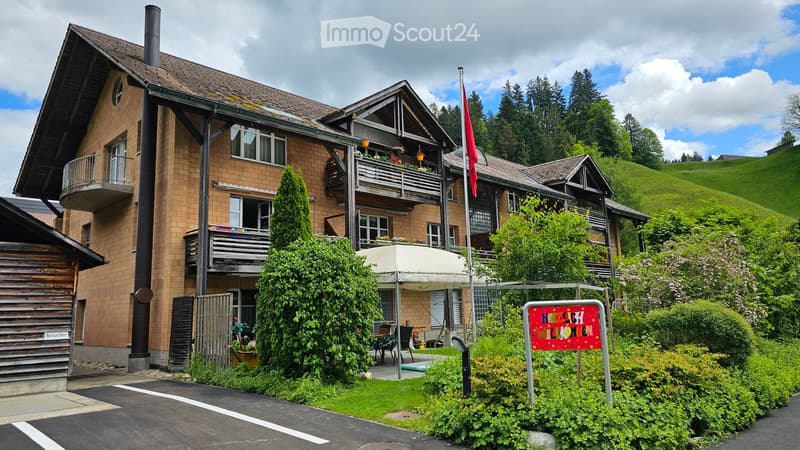 2 story house with brick facade, wooden balconies, green lawn, flag pole