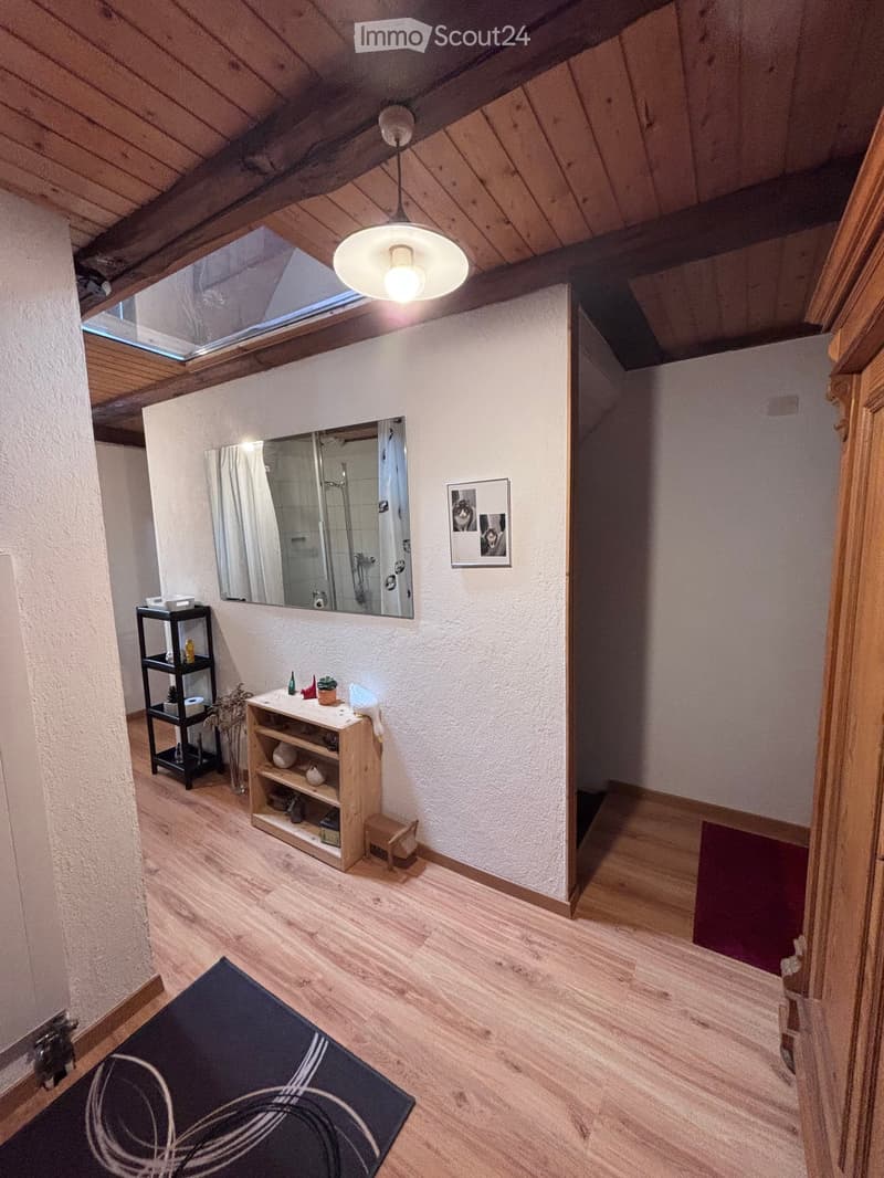 Bathroom with wooden flooring, a large mirror above the sink, a small wooden shelf, a black metal shelf, a picture frame on the wall, and a blue rug on the floor.
