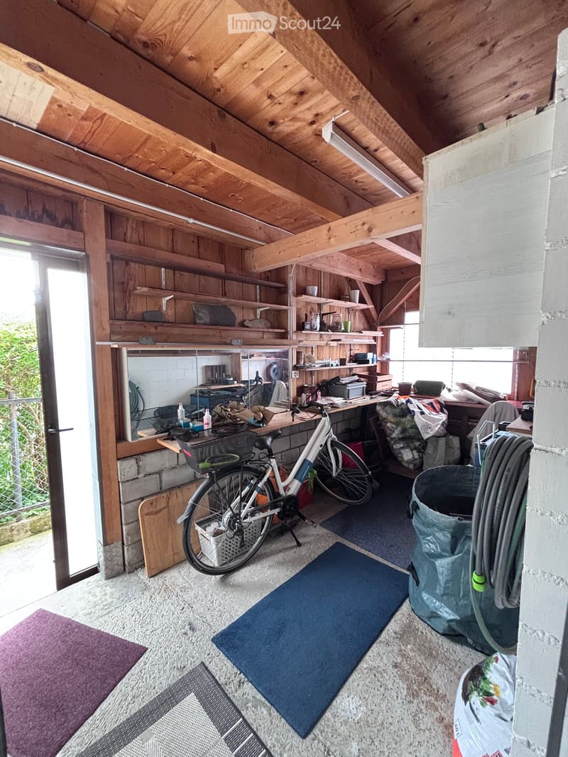 A wooden-framed attic or storage room with exposed beams, shelves, a bicycle, a desk, and various storage items.