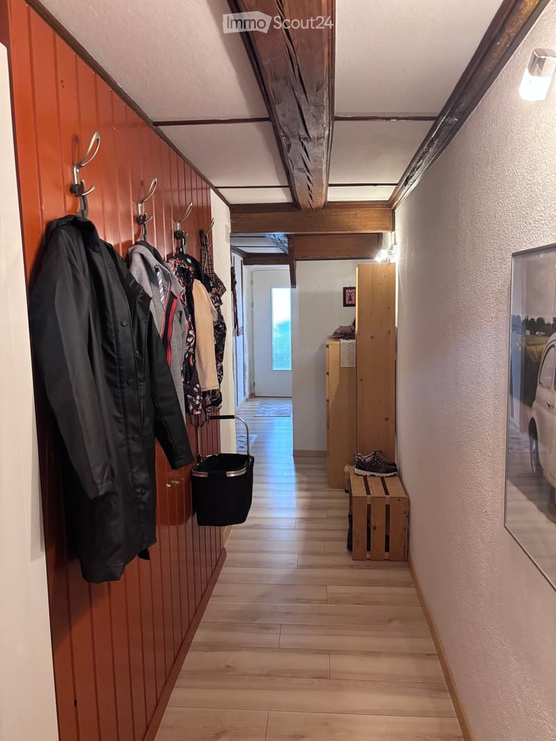 Wooden hallway with coat rack, mirror, and small bench. Wooden flooring and warm lighting.