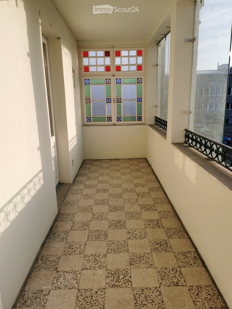 Balcony with tiled floor, white walls, decorative glass door, and metal railing.
